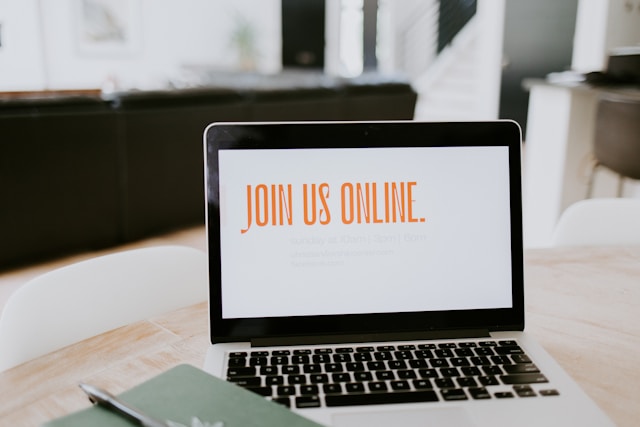 A MacBook on a table with its screen displaying “Join us online.”
