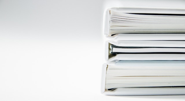 Close-up view of a stack of thick folders on a white surface.
