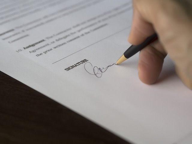 A hand appends a signature on a printed document.
