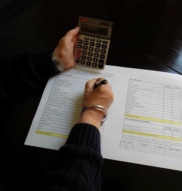 A hand holds a calculator and writes on the page of a printed document.
