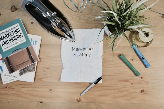 A white piece of A4 paper on a cluttered table has the phrase “Marketing Strategy.”
