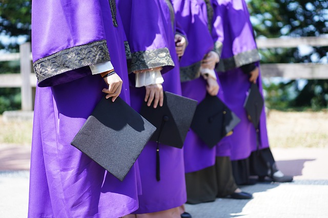 A group of people in graduation robes hold graduation hats.
