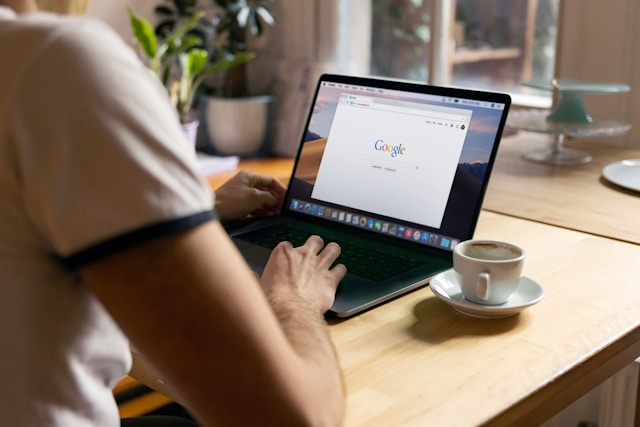 A person uses a black laptop to open a Google Chrome tab.
