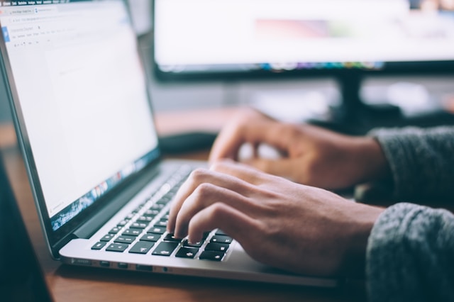 A hand presses the keys of a silver laptop.
