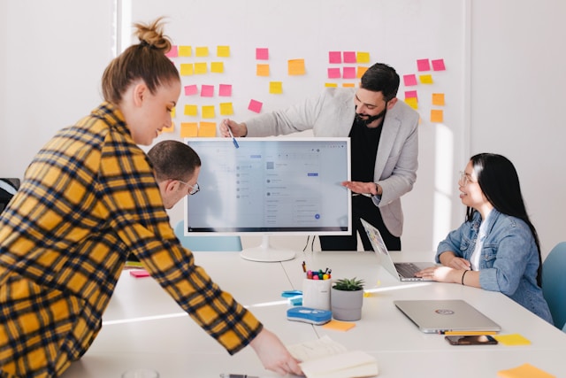 People work together in a meeting room with a large computer. 
