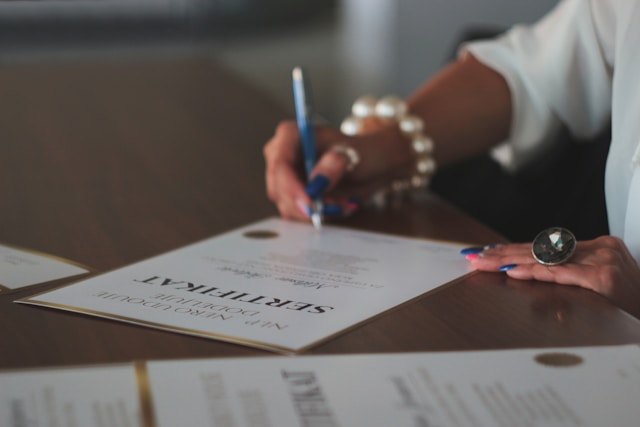 A blurry photo of a person who signs a certification document on a table. 
