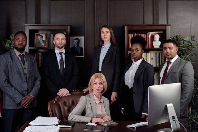 A group of professionals behind an office desk wearing formal suits.
