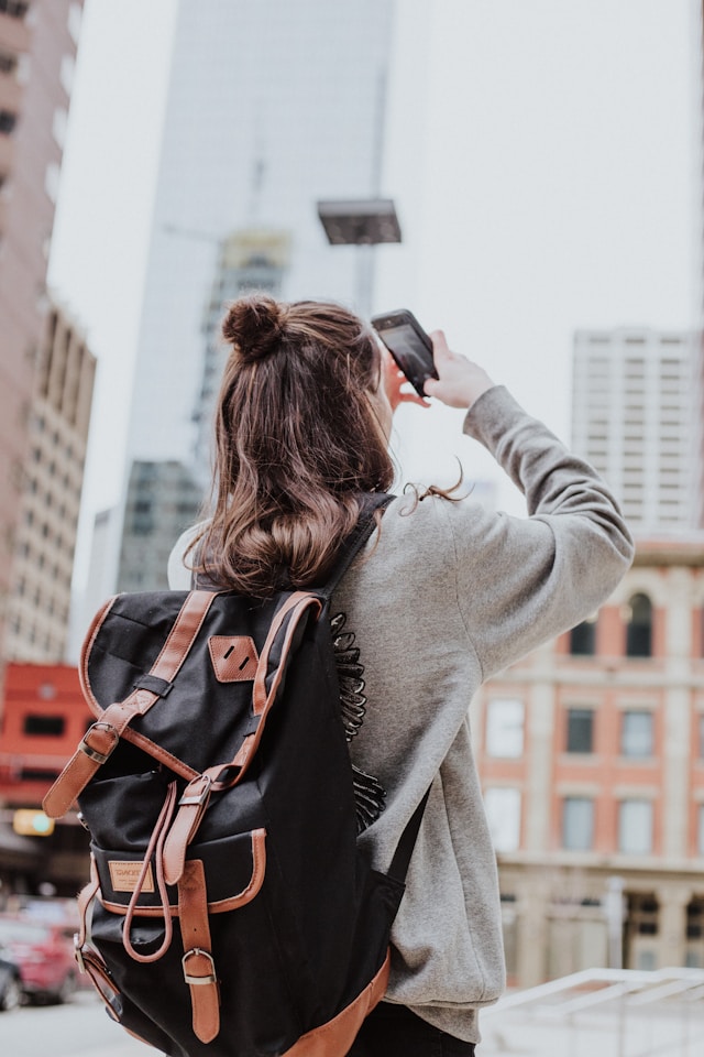 A person wearing a backpack uses their cellphone to take a picture of a billboard.