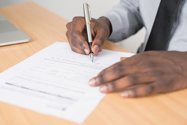What Is a Notarized Translation? Why Is It Important? 6 A person in a white shirt and a tie signs a document on a table.