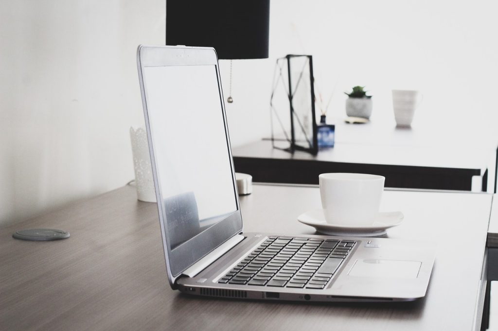 Translator Jobs Remote: A Guide to Work-From-Home Jobs 6 A silver laptop beside a white ceramic teacup on a wooden surface.