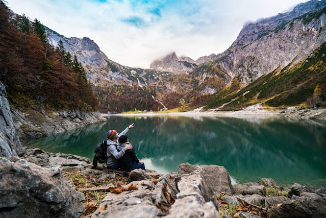 How To Marry a Non-US Citizen 6 Two people sit on a wooden plank by a lake surrounded by mountains.